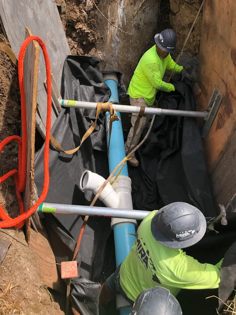 MIRA craftworker making a field connection on the hillside sewer project.