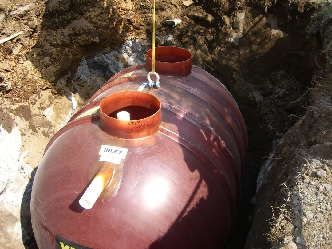 A large septic tank being lowered into an excavated trench.